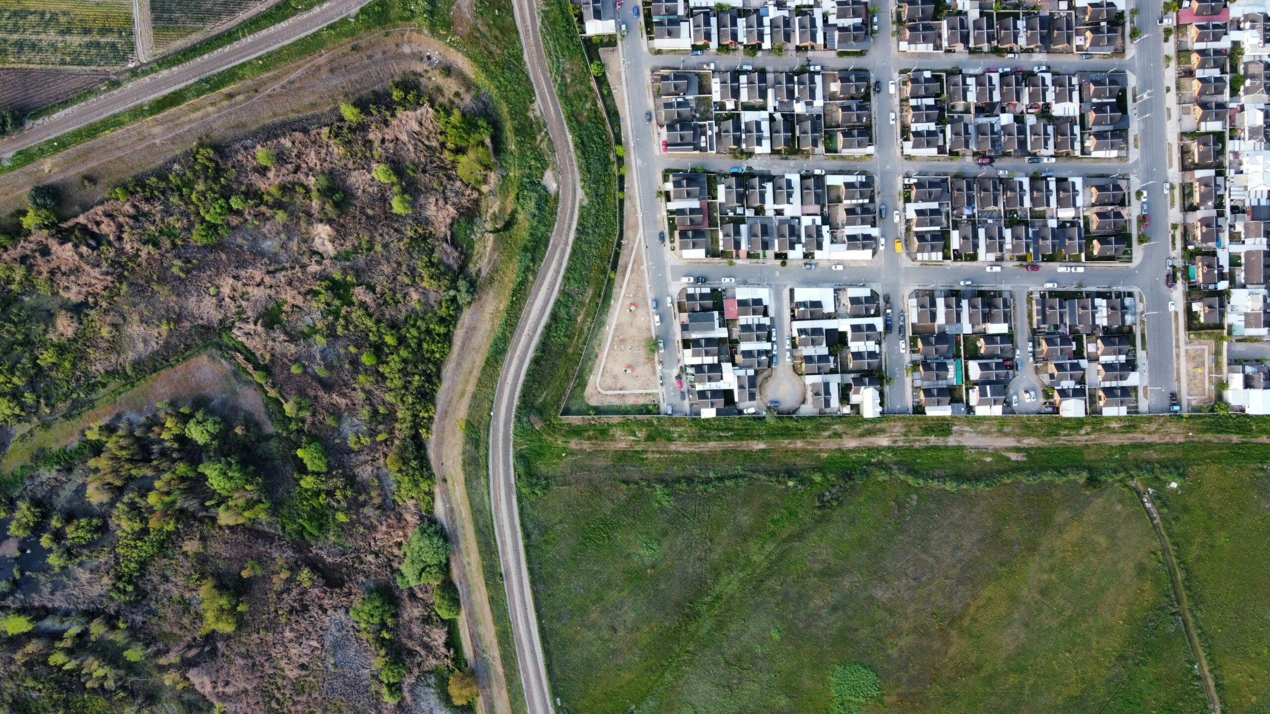 Drone view of a residential neighborhood alongside a natural landscape, showcasing urban and rural contrast.